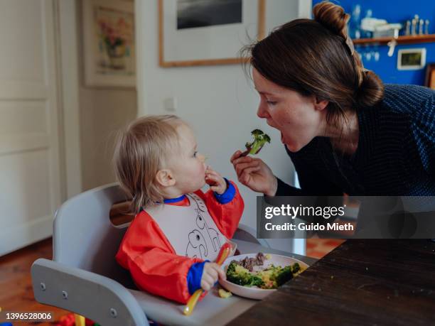 mother eating broccoli  in front of her amazed little girl. - child eat side stock-fotos und bilder