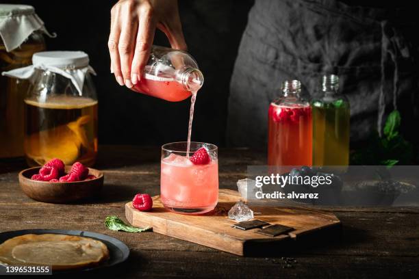 close-up of woman pouring raspberry kombucha tea in glass - kombucha stockfoto's en -beelden