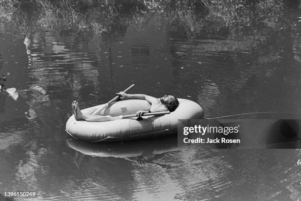 View of American composer and lyricist Stephen Sondheim as he sunbathes in an inflatable dinghy in the water, New Hope, Pennsylvania, mid 1970s.