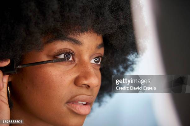 afro woman applying mascara on her eyelashes while doing her makeup. - wimperntusche stock-fotos und bilder