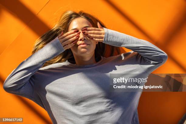 donna caucasica sdraiata sullo sfondo arancione e che si copre gli occhi - mani sugli occhi foto e immagini stock