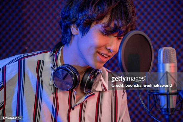 music, show business, people and voice concept - male singer with headphones and microphone singing song at sound recording studio - afl star stock pictures, royalty-free photos & images