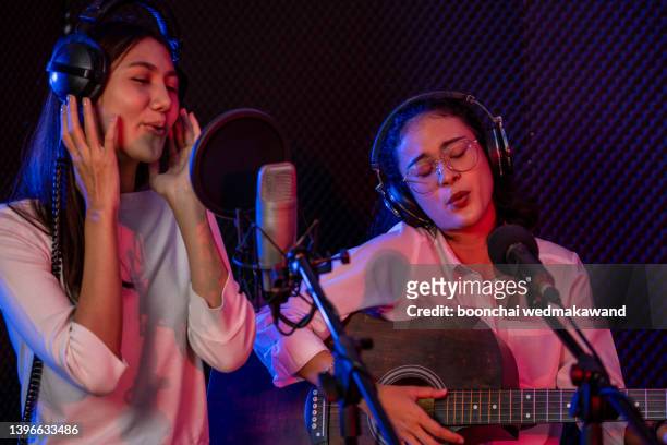 portrait of cheerful young woman, duet singing into a condenser microphone while recording a song in a professional studio - presentator amusement stockfoto's en -beelden