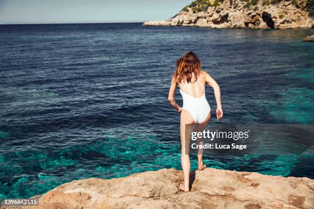 female in white swimsuit about to leap off into a turquoise sea - cliff shore stock pictures, royalty-free photos & images