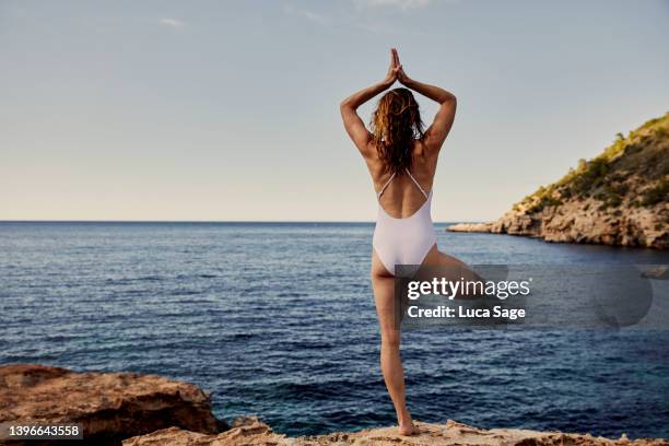 woman practising yoga looking out to beautiful ibizan sea - sistema immunitario foto e immagini stock