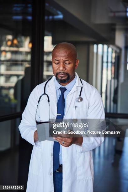 mature male doctor using a tablet in a hospital hallway - determination doctor stock pictures, royalty-free photos & images