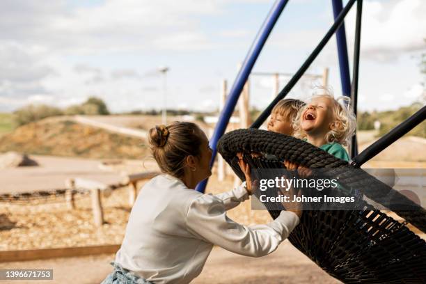 happy mother swinging children at playground - activity stock pictures, royalty-free photos & images