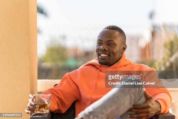 relaxed african american man enjoying a drink while sitting on a sofa outdoors. - familie sofa stock pictures, royalty-free photos & images