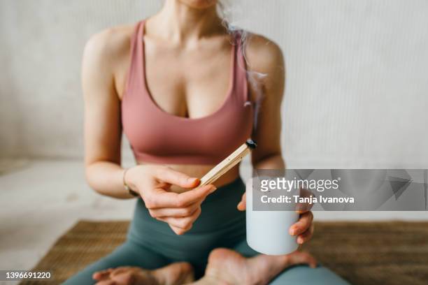 young woman lights a palo santo stick from a candle before meditation. the process of the ritual of fumigating a room for spiritual practice. - feierliche veranstaltung stock-fotos und bilder
