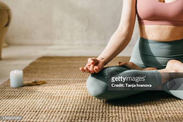 unrecognizable woman doing yoga at home. cropped image of a woman meditating in the lotus pose with incense burning next to her - mudra stock-fotos und bilder