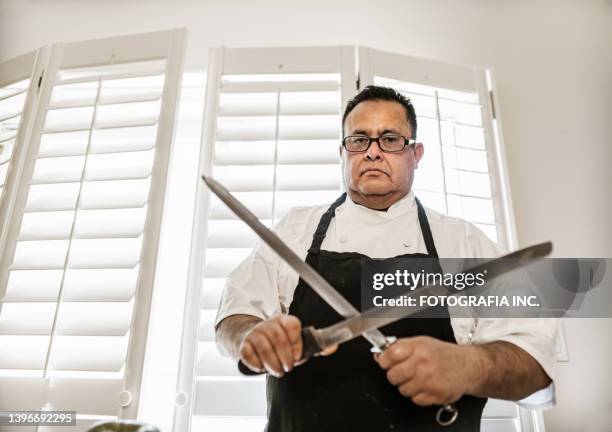 mature latin chef sharpening kitchen kinfe - kinfe stock pictures, royalty-free photos & images