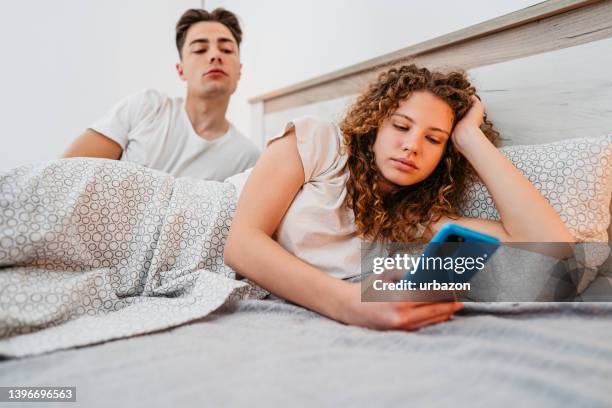 boyfriend spying on his girlfriend while she uses smart phone - betrayal stock pictures, royalty-free photos & images