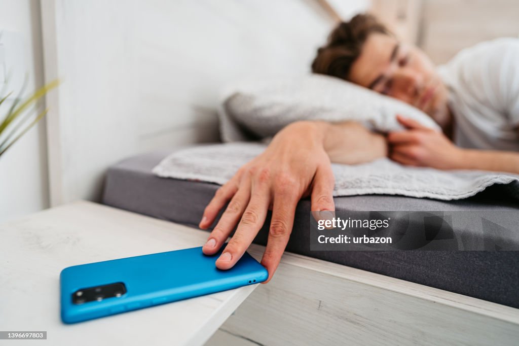Young Man Snoozing Alarm On A Smart Phone