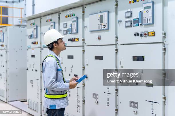 engineer working at switch panel of switchgear room, young electrician working at electrical room with tablet, industrial service engineer checking conducts of control panel at power plant, energy - schaltschrank stock-fotos und bilder