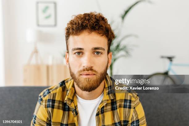 confident hipster young gay man looking at camera while relaxing on sofa at home - portrait of trendy guy - elegant handsome beard man foto e immagini stock