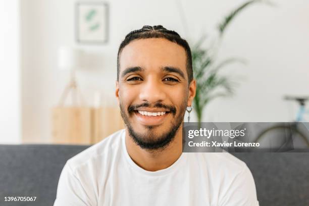 joyful hispanic latino young woman smiling at camera while sitting on sofa in the living room at home - portrait of happy venezuelan guy - venezuelans stock pictures, royalty-free photos & images