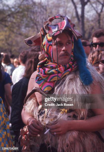 View of a shirtless man, a mask atop his head, a scarf around his neck, and a fur sash over one shoulder, as he attends the first Earth Day event,...