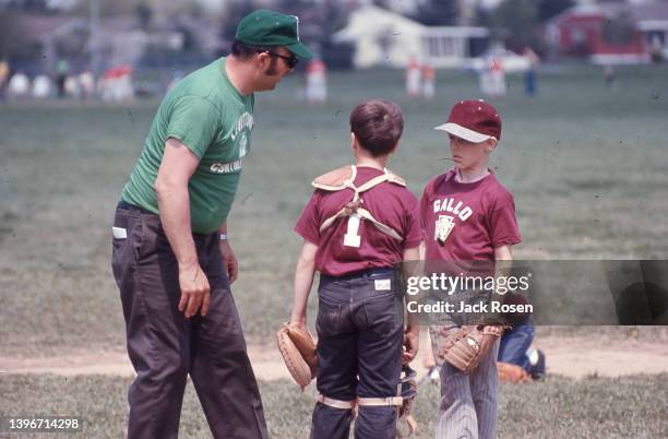 An unidentified coach talks with two young baseball players , one a catcher and the other a pitcher, during a Levittown Continental Little League...