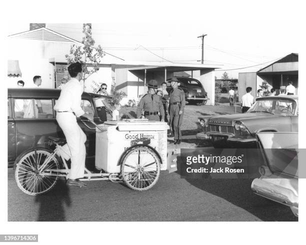 View of a Good Humor ice cream vendor as he bicycles though the Dogwood Hollow neighborhood, past Pennsylvania State Police officers who had been...