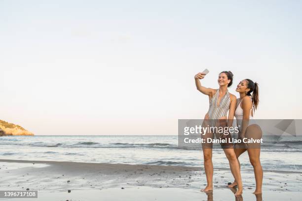 two female friends taking a selfie with a mobile phone while enjoying a day at the beach. - beach photos stock-fotos und bilder