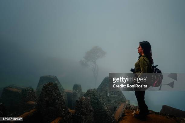 woman from behind with backpack looking at the ruins of machu picchu with fog - ancient civilisation inca stock pictures, royalty-free photos & images