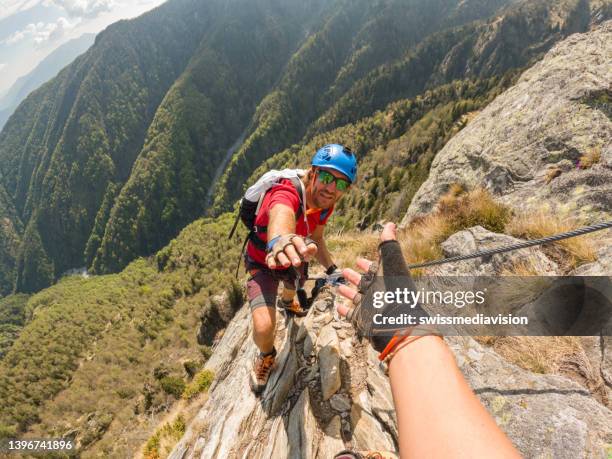 pov down arm to young man climbing up a rock face - redding sporten stockfoto's en -beelden