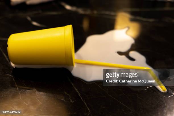 don’t cry over spilled milk: bright yellow cup & straw overturned on counter with milk splattered - spilt milk foto e immagini stock