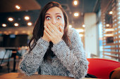 Shocked Woman Covering Her Mouth Sitting in a Restaurant