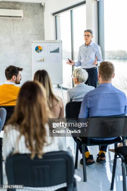 mid adult ceo, der seinen kollegen eine geschäftspräsentation am whiteboard im büro gibt. - education retirement stock-fotos und bilder