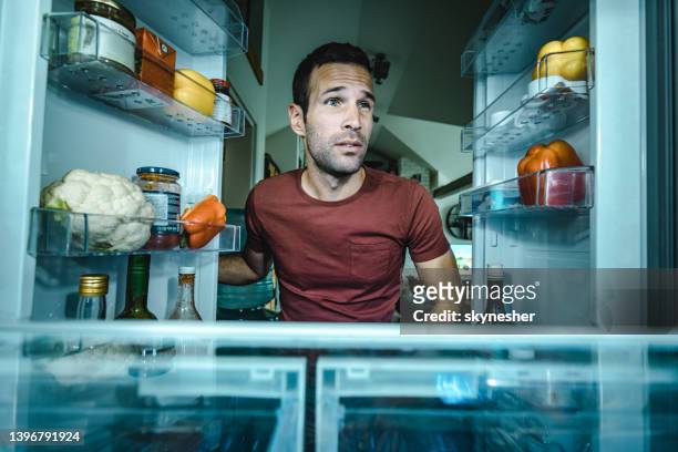 young man looking at half-empty fridge in the kitchen. - refrigerator imagens e fotografias de stock