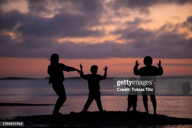 silhouetted family dancing, gesturing on ocean beach at sunset - tobias materna imagens e fotografias de stock