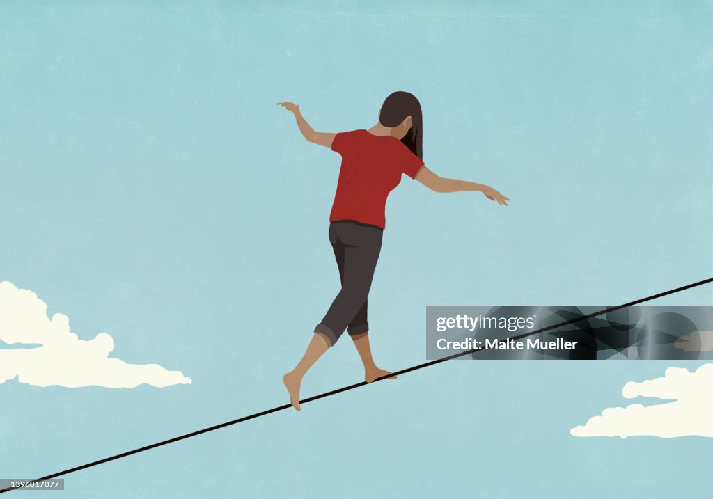 Barefoot woman walking along tightrope in sky