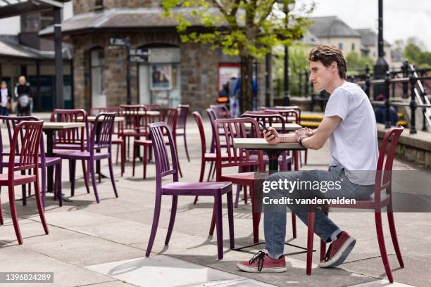 man in his 30s sitting outdoors texting - khaki pants sitting stock pictures, royalty-free photos & images