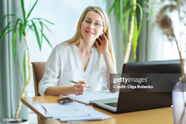smiling blond woman looking at camera holding a pen, working at office - copy editor stock pictures, royalty-free photos & images