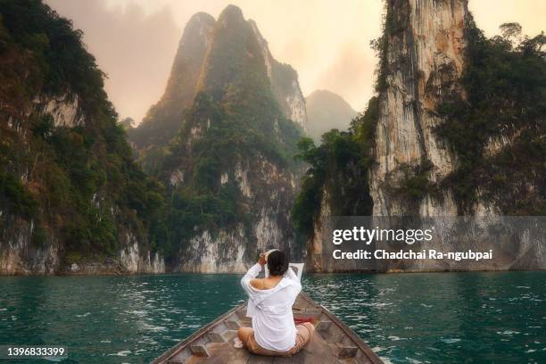 travel woman taking a picture with a smartphone on traditional longtail boat with beautiful scenery view in ratchaprapha dam at khao sok national park - thailand stock-fotos und bilder