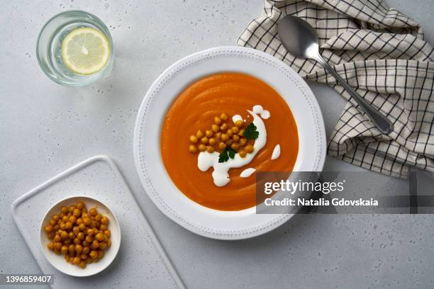 top view of pureed pumpkin fall soup with chick-peas and coconut cream served with glass of lemon water and cutlery on table, horizontal, flat lay. delicious healthy dieting food for vegetarians. hearty lunch - pumpkin soup stock-fotos und bilder