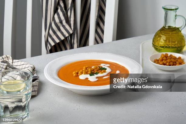autumn pumpkin pureed soup with chickpeas and coconut cream served on plate. olive oil, glass of water, dinning table. dieting ready-to-eat meal for vegans. healthy eating concept. side view, horizontal - cremesuppe stock-fotos und bilder