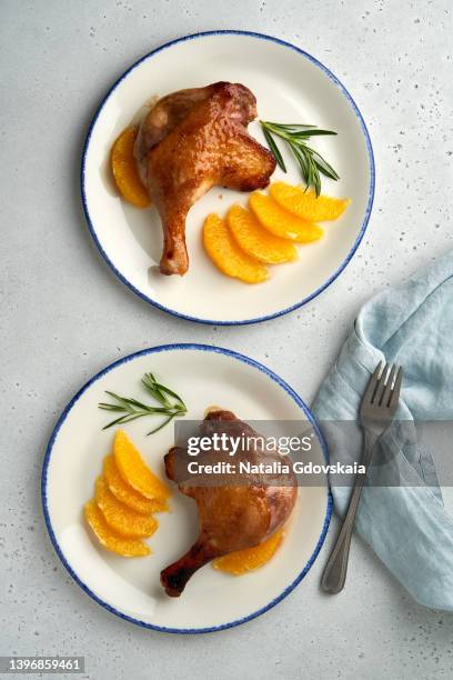 two plates of roasted duck confit with tangerine and rosemary, paleo diet eating, juicy meat with crispy crust, citrus flavor of mandarin duck meal, vertical, top view. full of dietary fiber, tender legs, paleo diet concept - confit stock pictures, royalty-free photos & images