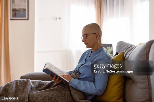 woman living with cancer, reading a book at home - rest cure stock pictures, royalty-free photos & images