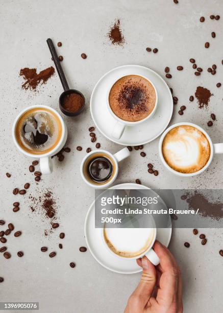 cropped hand of person holding coffee cup by by scattered beans and powder on table - chocolate powder stock-fotos und bilder