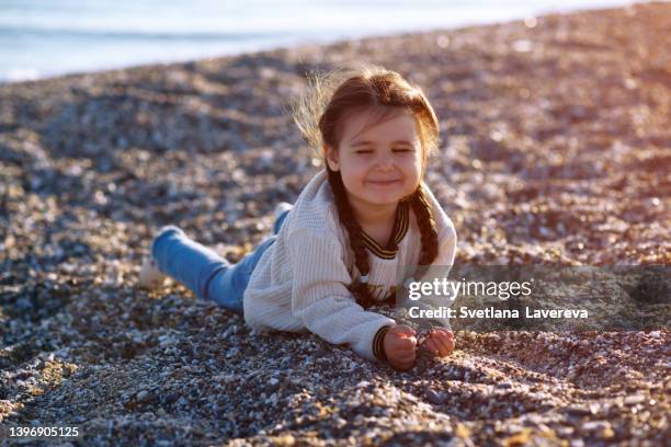 cute portrait of little toddler child playing with sea shells and stones on sandy beach. girl picking up shells and holding them in hand. - kid middle finger stock-fotos und bilder