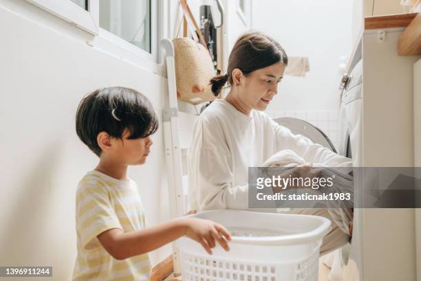 若い母親が洗濯機に服を運び込む少年 - housework ストックフォトと画像