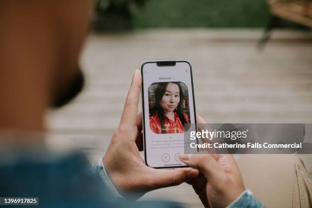 a man holds a smart phone and browses a dating app - ersuchen stock-fotos und bilder