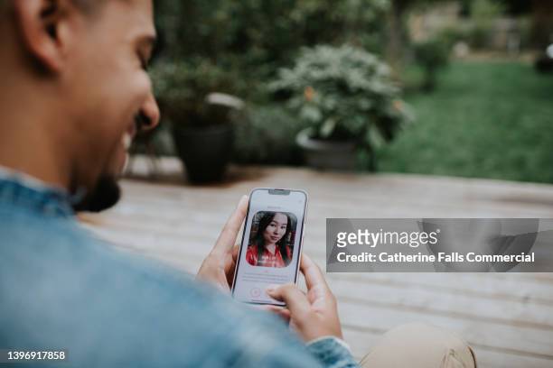 a man holds a smart phone and browses a dating app - dating app photos et images de collection
