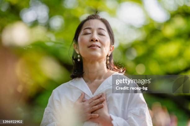 woman meditating in nature - smiling with hands on chest stock pictures, royalty-free photos & images