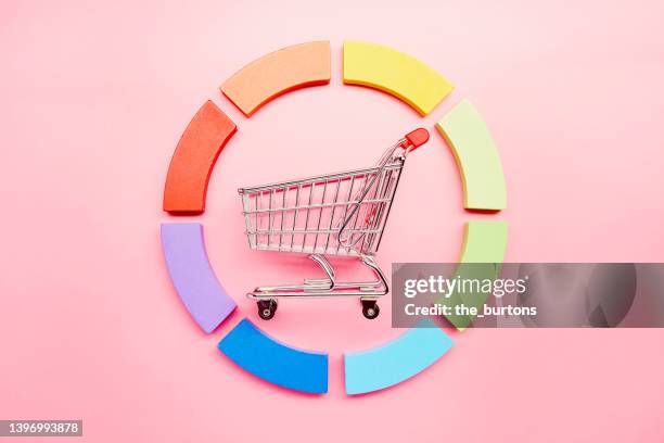 pie chart made of colorful building blocks and a small shopping cart on pink background - cake sale stock-fotos und bilder