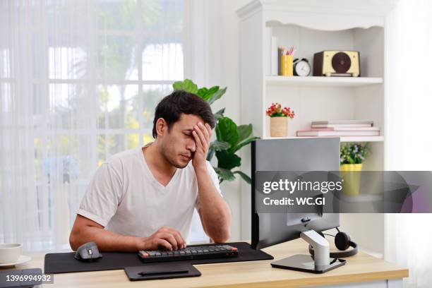 tired male working at home using a computer and uses his hand to close his eyes looking anxious. - rubbing eyes stock pictures, royalty-free photos & images