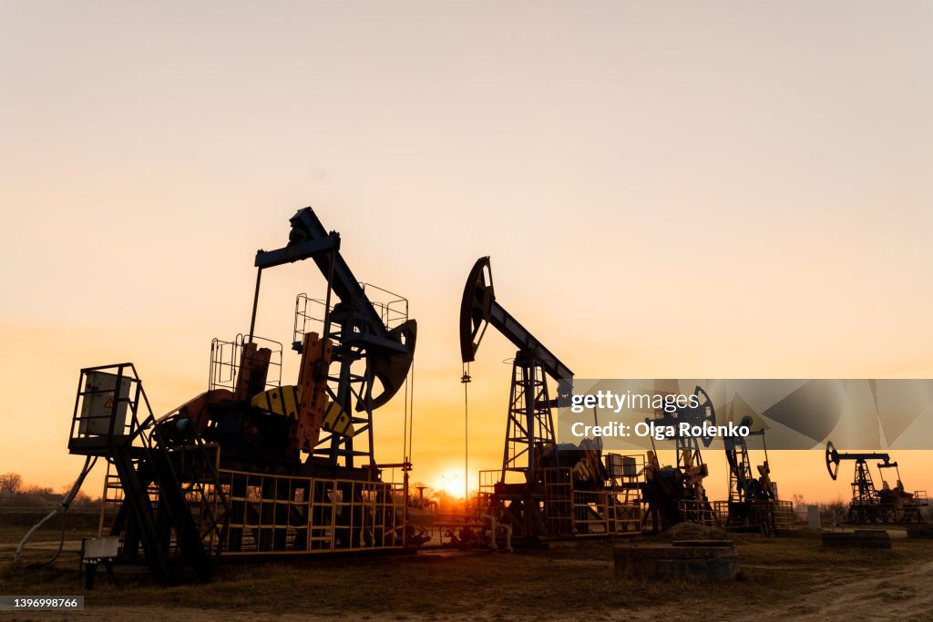 The silhouette of five oil pumps on a beautiful sunset sky with sun setting in between them.Siberia. Oil and gas production