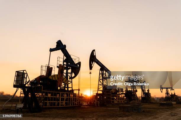 the silhouette of five oil pumps on a beautiful sunset sky with sun setting in between them.siberia. oil and gas production - piattaforma petrolifera foto e immagini stock