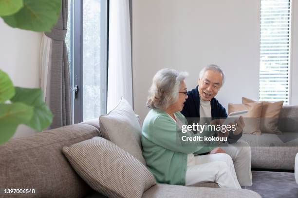 vue latérale d’un couple asiatique âgé utilisant une tablette numérique à la maison. - elderly care japanese photos et images de collection